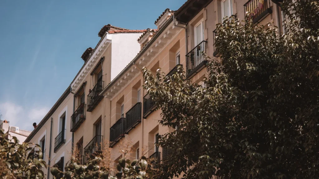 Fachadas de edificios de viviendas con balcones de hierro en una calle de Madrid, con árboles delante