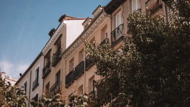 Fachadas de edificios de viviendas con balcones de hierro en una calle de Madrid, con árboles delante