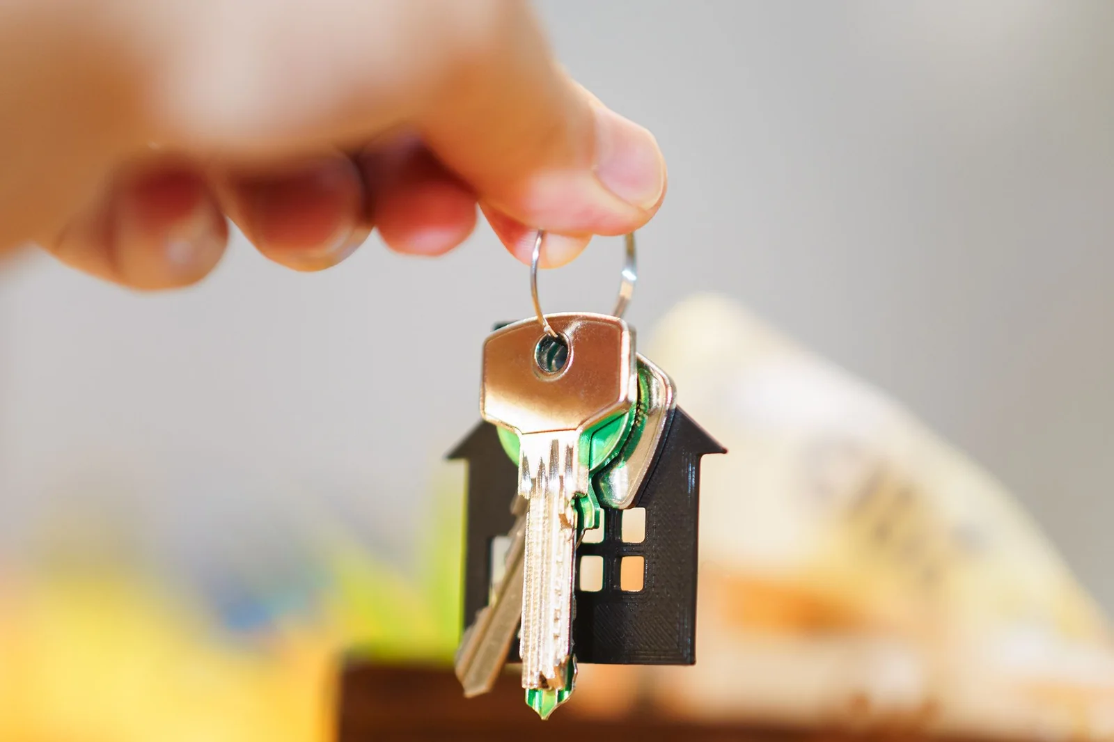 Mano que sostiene unas llaves con llavero en forma de casa sobre una cartera y una maqueta de casa